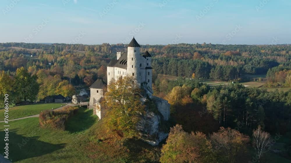 The grand silhouette of a medieval fortress towers over a forest ablaze with autumn's vibrant colors. Bobolice, Polish Jura, Polish Jurrasic Haighland, Poland The grand silhouette of a medieval fortress towers over a forest ablaze with autumn's vibrant colors. Bobolice, Polish Jura, Polish Jurrasic Haighland, Poland