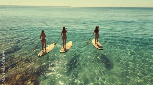Three happy women stands on a sup boards. In the background, the ocean and the sunset