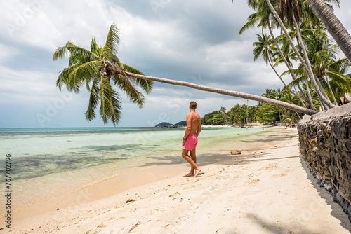 Mężczyzna w kąpielówkach na rajskiej plaży pod palmą © DawidFastMan
