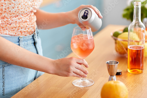drinks and people concept - close up of woman pouring soda from tin can to wine glass and making orange cocktail at home kitchen