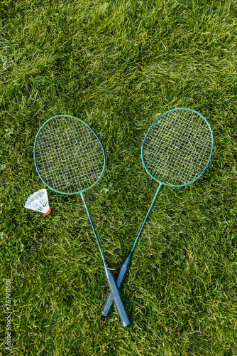 leisure games and sport equipment concept - close up of badminton rackets and shuttlecock on grass