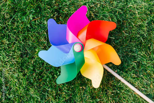 ecology, environment and sustainable energy concept - close up of multicolored pinwheel on green lawn or grass