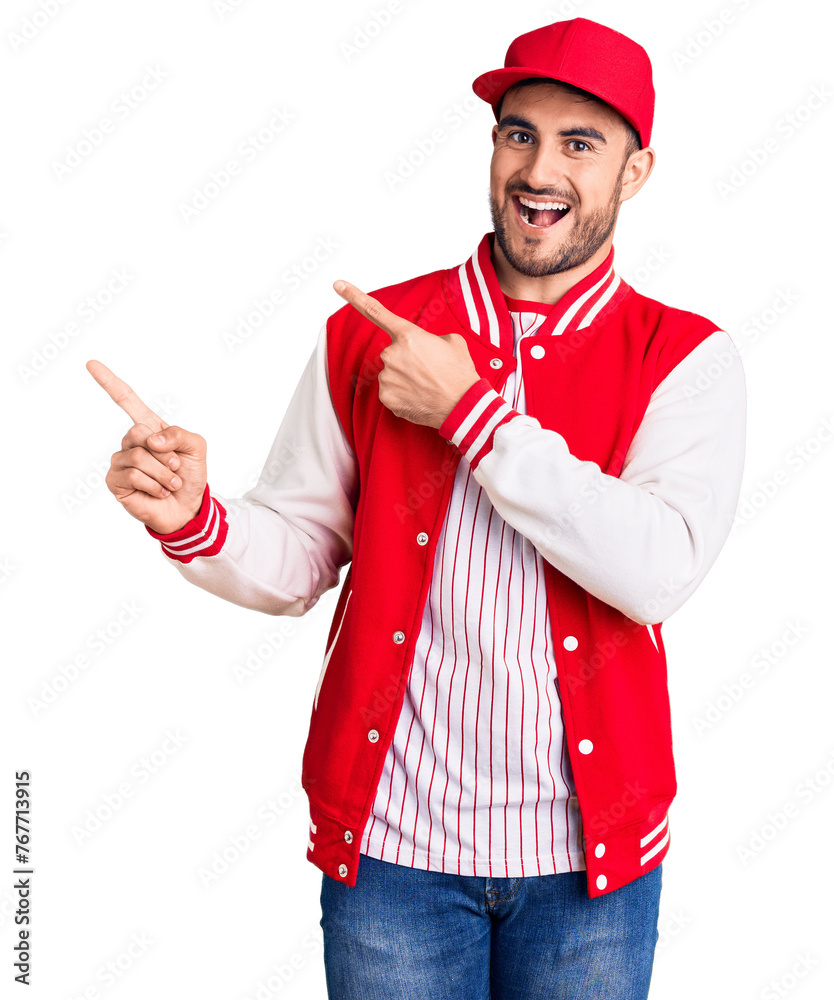 Young handsome man wearing baseball jacket and cap smiling and looking at the camera pointing with two hands and fingers to the side. Young handsome man wearing baseball jacket and cap smiling and looking at the camera pointing with two hands and fingers to the side.