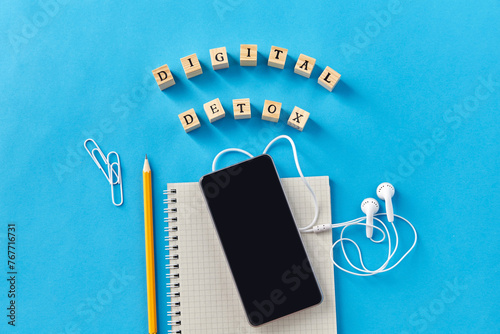 digital detox and technology concept - smartphone, earphones and wooden toy block or stamps on blue background