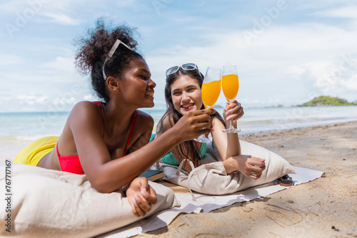 Two women are laying on a beach, holding glasses of orange juice and smiling