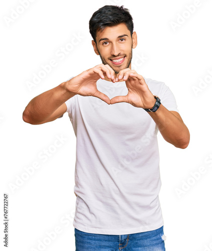 Young handsome man wearing casual white tshirt smiling in love doing heart symbol shape with hands. romantic concept.