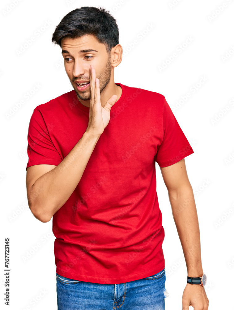 Young handsome man wearing casual red tshirt hand on mouth telling secret rumor, whispering malicious talk conversation Young handsome man wearing casual red tshirt hand on mouth telling secret rumor, whispering malicious talk conversation