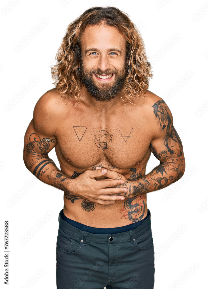 Fototapeta premium Handsome man with beard and long hair standing shirtless showing tattoos smiling and laughing hard out loud because funny crazy joke with hands on body.