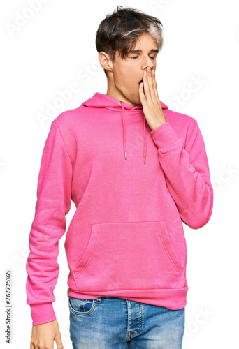 Young hispanic man wearing casual pink sweatshirt bored yawning tired covering mouth with hand. restless and sleepiness.