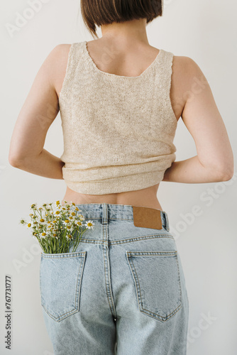 Young pretty woman with chamomile flowers bouquet in jeans pocket. Backside view