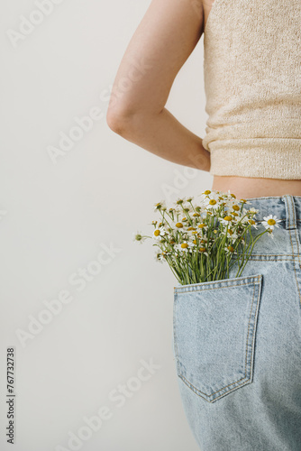 Young pretty woman with chamomile flowers bouquet in jeans pocket