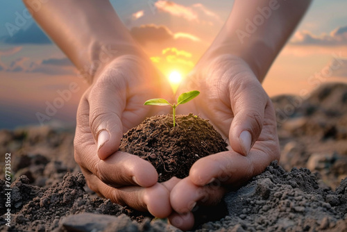 Hands cradling a handful of earth, from which a tiny sapling emerges, against a backdrop of a rising sun, symbolizing the dawn of a new era of environmental awareness on Earth Day photo