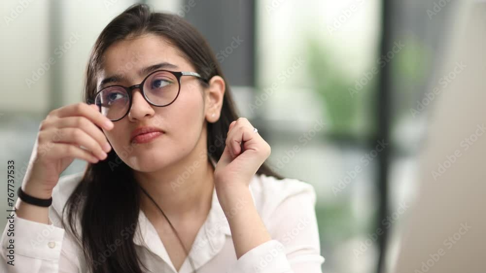 Young businesswoman expressing misunderstanding or tiredness while sitting by desk in front of laptop and looking through online data