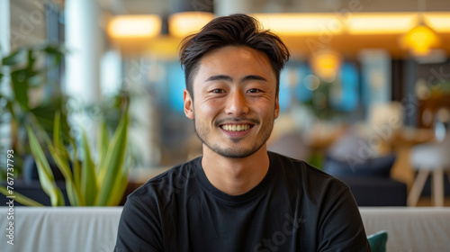 a happy 30 year-old Japanese man with a modern hipster haircut, wearing a black t-shirt sitting in a ultra modern office with white furnishings and brightly colored