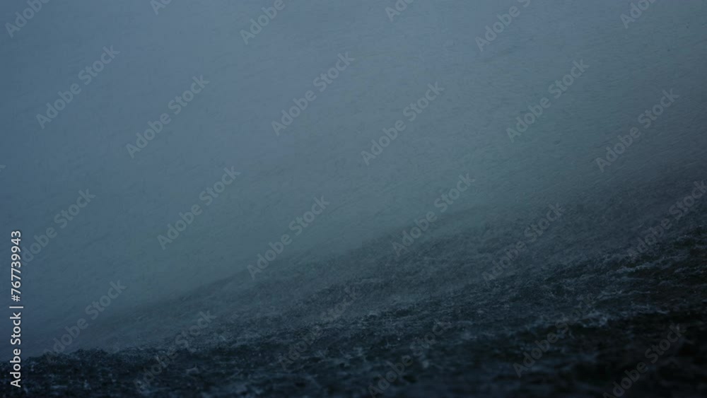 Ocean water spray and mist blows over top of wave on stormy day, slow motion in water