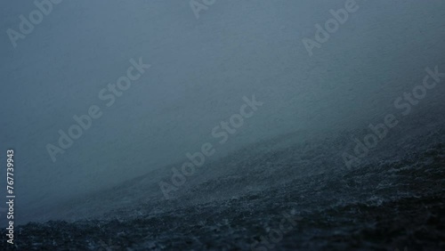 Ocean water spray and mist blows over top of wave on stormy day, slow motion in water