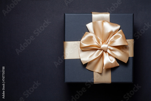 Black gift box with champagne gold ribbon bow on a black background. top view