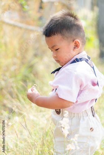 A Thai Southeast Asian toddler is picking and looking at flowers on the side of the road.