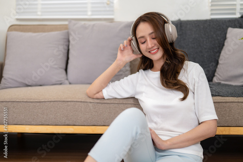 Young woman enjoying her vacation Listen to her favorite songs while relaxing in the living room at home. © Wasana