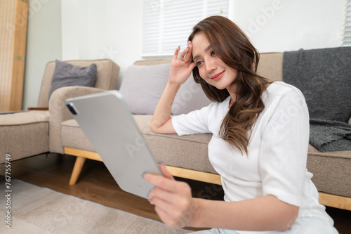 young woman sitting in living room, watching movies on digital tablet, reading on device, enjoying weekend at home