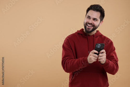 Happy young man using smartphone on beige background, space for text © New Africa
