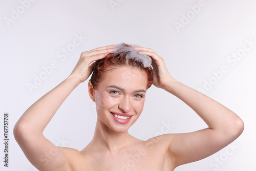 Happy young woman washing her hair with shampoo on light grey background