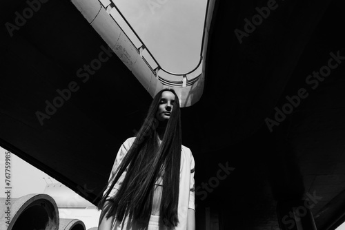Beautiful long-haired girl posing under a bridge over which cars drive, black and white photography