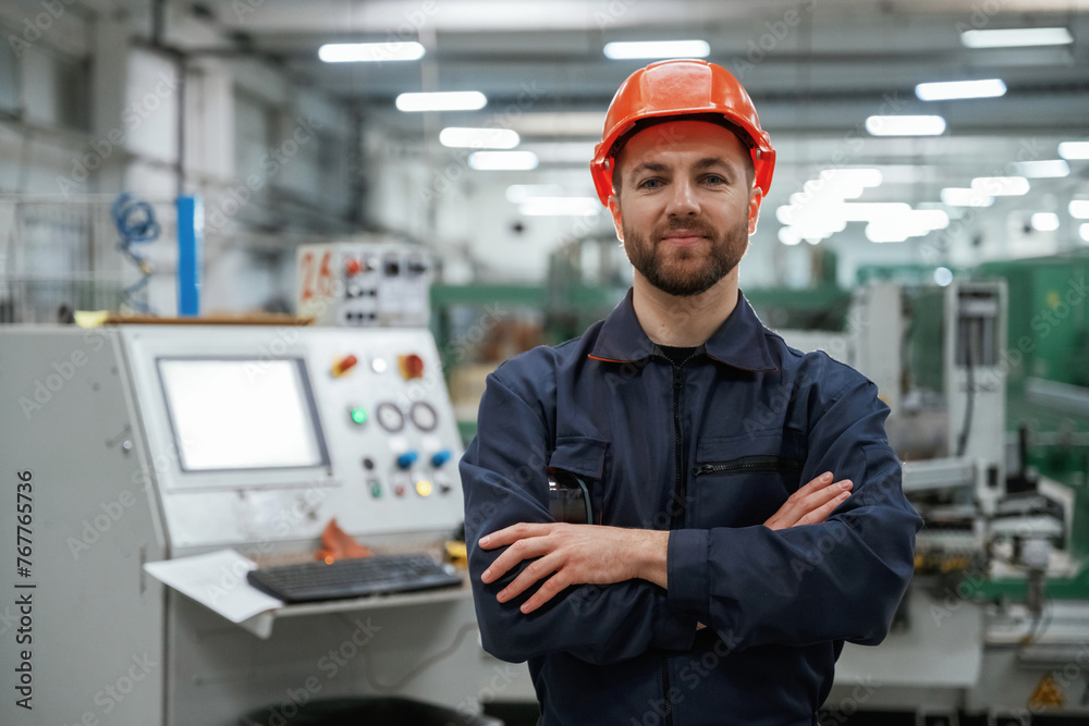 Standing with arms crossed. Factory worker is indoors with hard hat Standing with arms crossed. Factory worker is indoors with hard hat
