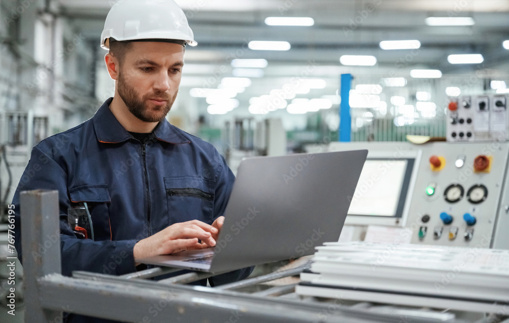 Using the laptop. Factory worker is indoors with hard hat Using the laptop. Factory worker is indoors with hard hat