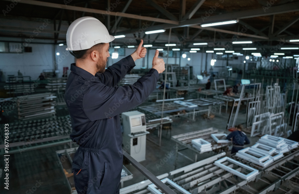 Gesture of thumb up. Factory worker is indoors with hard hat