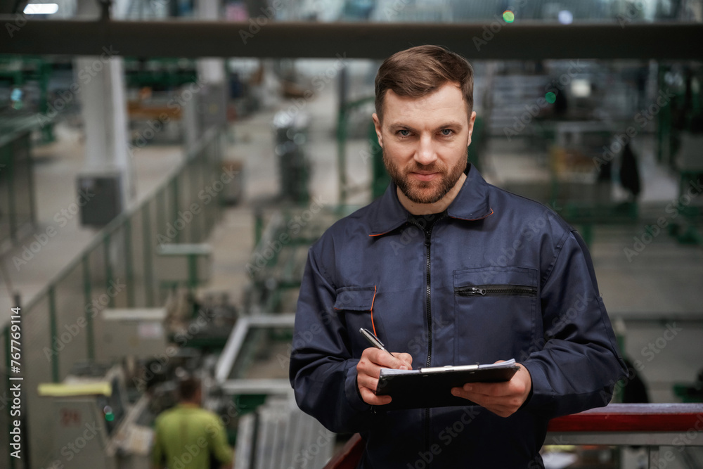 Writing information into the notepad. Factory worker is indoors with hard hat Writing information into the notepad. Factory worker is indoors with hard hat