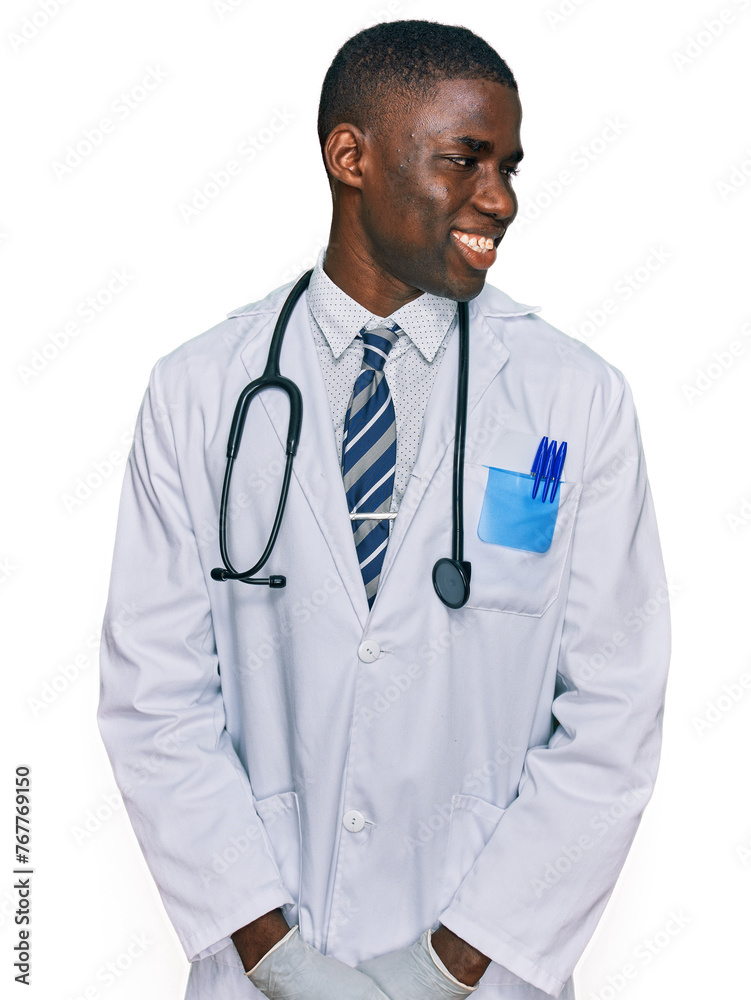 Young african american man wearing doctor uniform and stethoscope looking away to side with smile on face, natural expression. laughing confident. Young african american man wearing doctor uniform and stethoscope looking away to side with smile on face, natural expression. laughing confident.