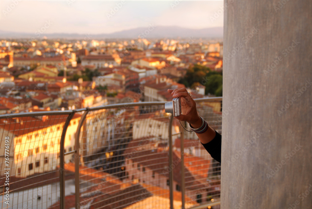 A hand holding a camera against the backdrop of a city view in sunset light
