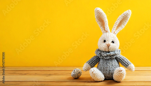 Closeup of a cute knitted easter bunny sitting on a wooden table against a yellow background with copy space and easter egg. Template for an Easter greeting card. Generative Ai.