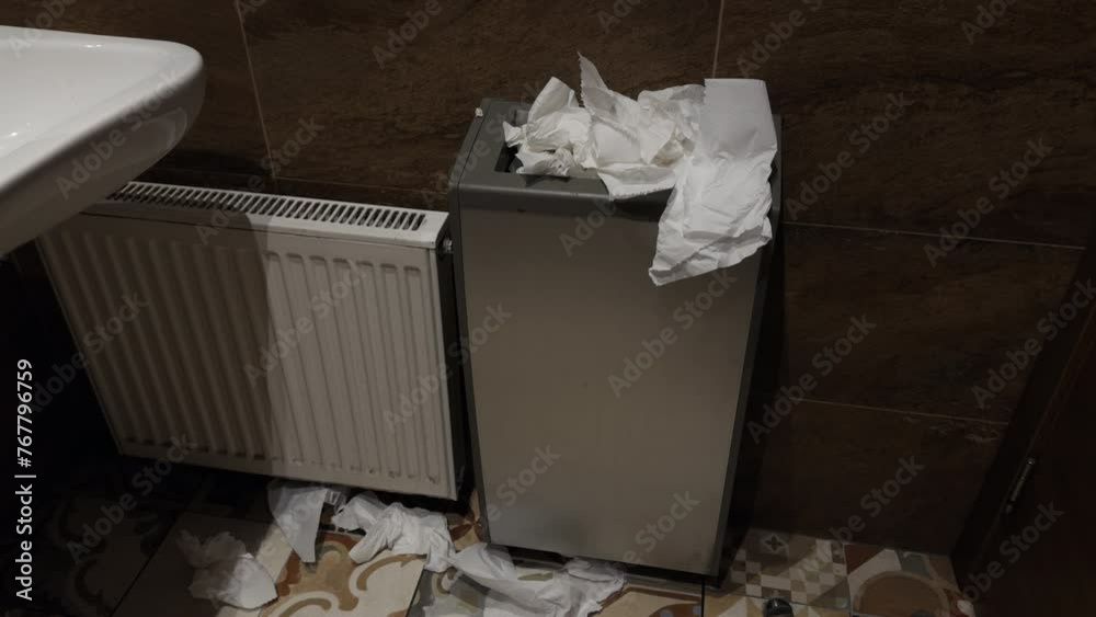 Overflowing trash can filled with dirty tissues on bathroom floor beside radiator Overflowing trash can filled with dirty tissues on bathroom floor beside radiator