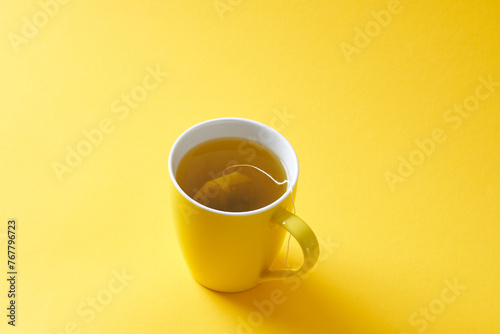 Tea bag in a yellow mug on a yellow background.
