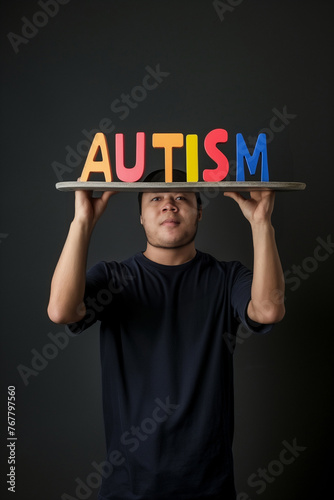 Young autistic man holding a sign with the word AUTISM written in large colored 3D letters, communication about people on the autistic spectrum, a neuroatypical, neurodivergent person photo