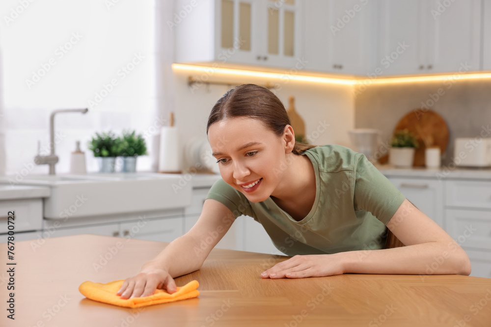 Woman with microfiber cloth cleaning wooden table in kitchen Woman with microfiber cloth cleaning wooden table in kitchen