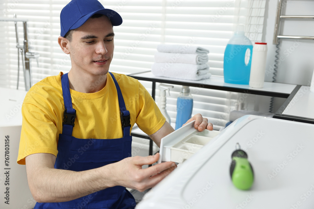Young plumber pulling detergent drawer out of washing machine in bathroom Young plumber pulling detergent drawer out of washing machine in bathroom