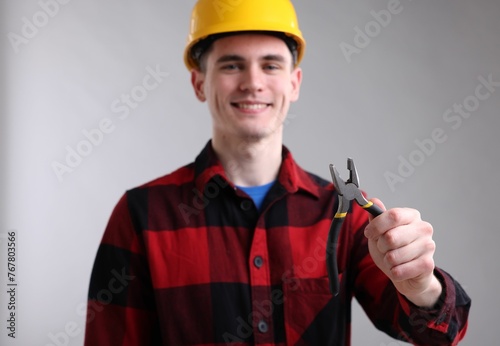 Young man holding pliers on grey background, selective focus