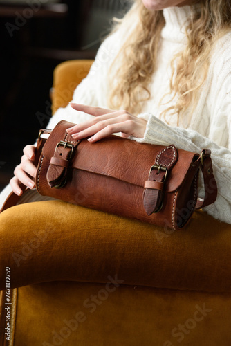 beautiful curly blond hair woman posing with a small tube brown bag in a vintage chair
