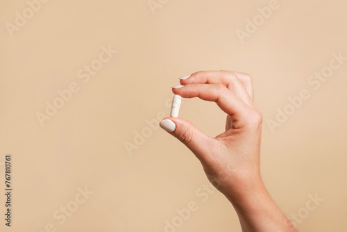 White pill in female hand on beige background, Taking Your Medication