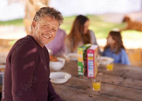 Portrait, mature and man with smile for picnic with family in nature of backyard of house and outdoor. Women, men and child eating breakfast on table of wood in summer, happiness and love in home