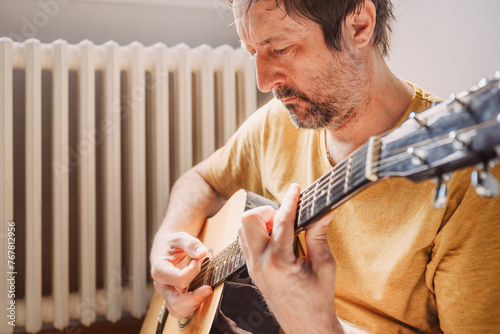 Lonely mid adult male playing acoustic guitar at home photo