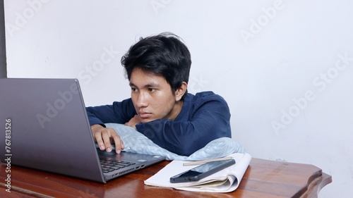 young asian male student tired, bored, studying too hard is studying on laptop, doing assignments