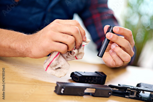 Hands, cleaning and man with gun at table for safety, self defense and handgun assembly. Process, equipment and person with firearm maintenance with cloth, magazine and wiping dust, dirt and oil