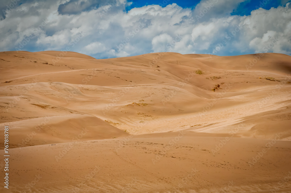 A serene image highlighting sprawling sand dunes with subtle textures, under a sky full of fluffy clouds, evoking a sense of calm