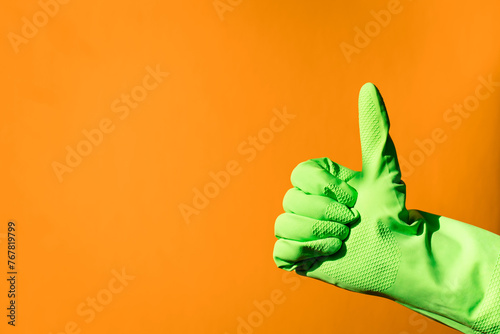 house cleaning concept. hand in green rubber household glove shows gesture super - thumbs up on orange background © Natalia