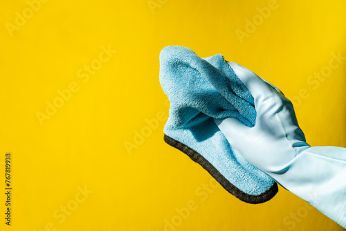 house cleaning concept. hands in blue rubber household gloves hold rag on yellow background. © Natalia