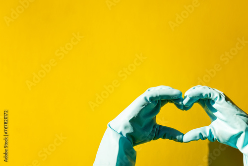 house cleaning concept. hand in blue rubber household glove shows gesture heart on yellow background. © Natalia